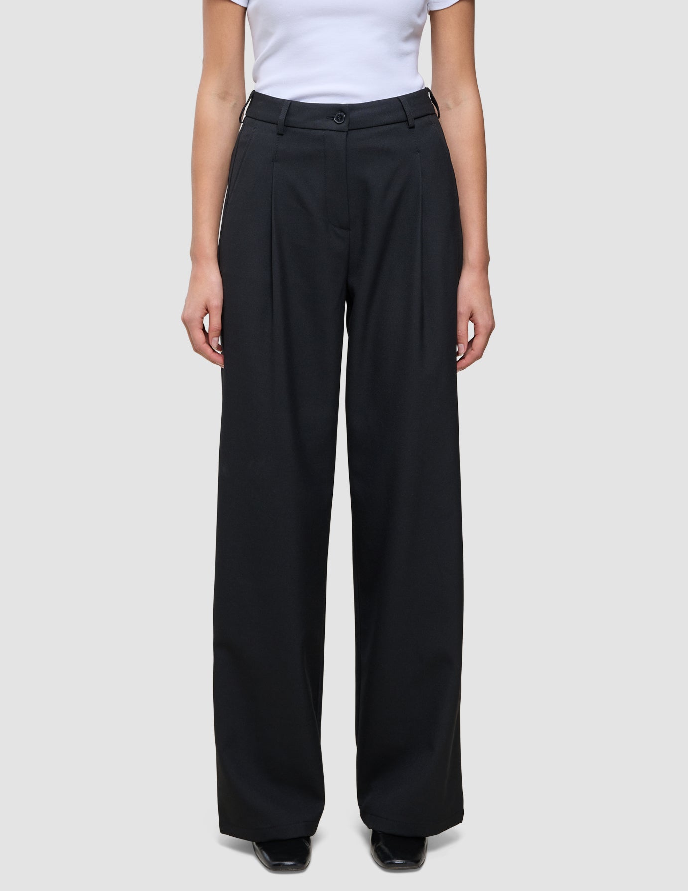 Person iført en hvid T-shirt og et par Serene Pants Wide Black med læg foran.