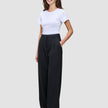 En smilende kvinde har en hvid T-shirt på og et par Serene Pants Wide Black med brede ben, og hun har en hånd i lommen.