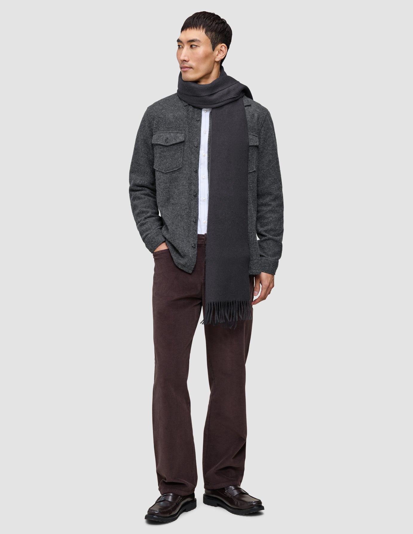 En mand er klædt i et afslappet og gennemtænkt outfit bestående af en hvid skjorte, mørke bukser, et antracitgråt tørklæde og loafers.