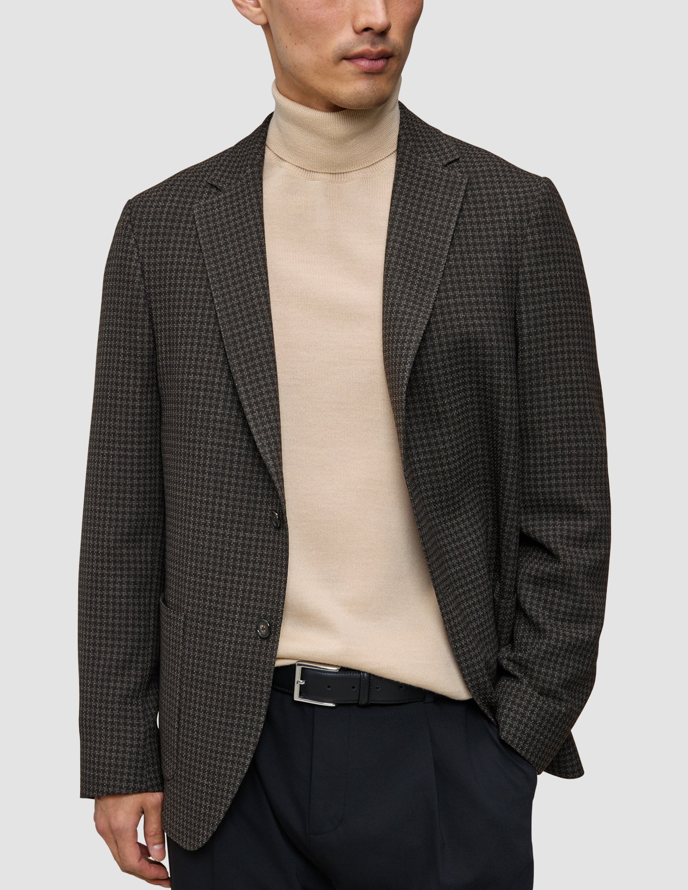 En mand iført et look bestående af strik og blazer med en mønstret uldblazer, mørke bukser og et sort bælte.