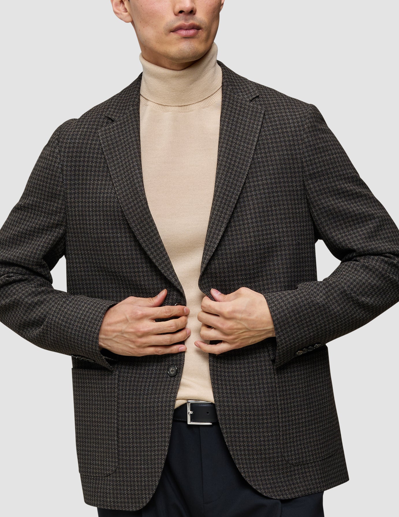 En person iført et look bestående af strik og blazer, med en merino-trøje med rund hals under en mørk, mønstret uldblazer.