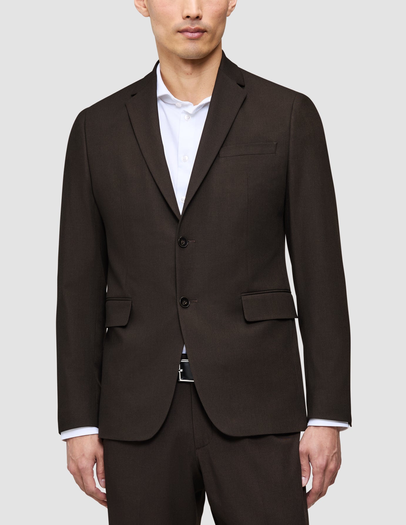 En mand iført en mørkebrun The suit that does it all-jakke over en eksklusiv hvid skjorte med krave.