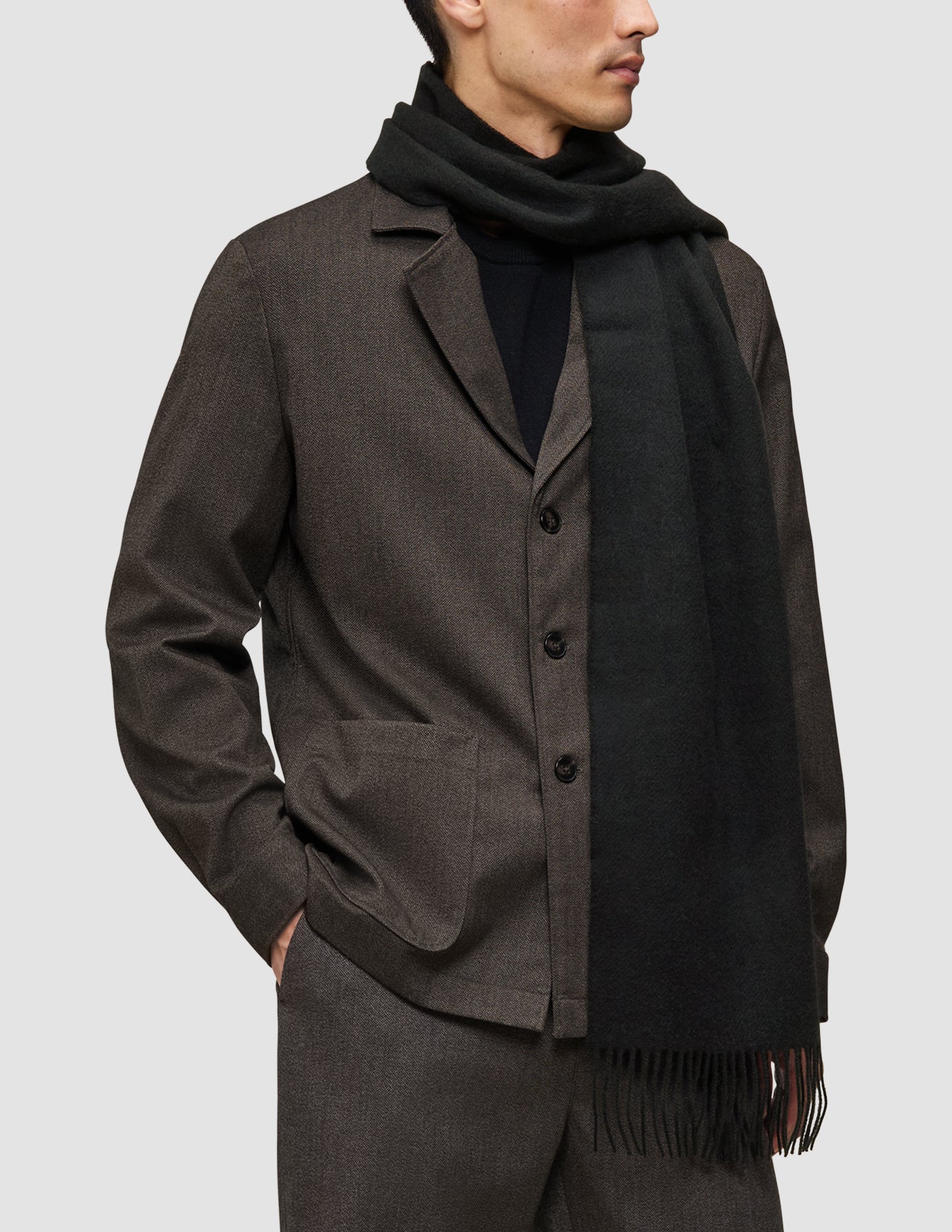 En mand iført et lidt anderledes sæt tøj: en brun Atelier Overshirt over en sort Premium Merino Knit-trøje og et tørklæde.