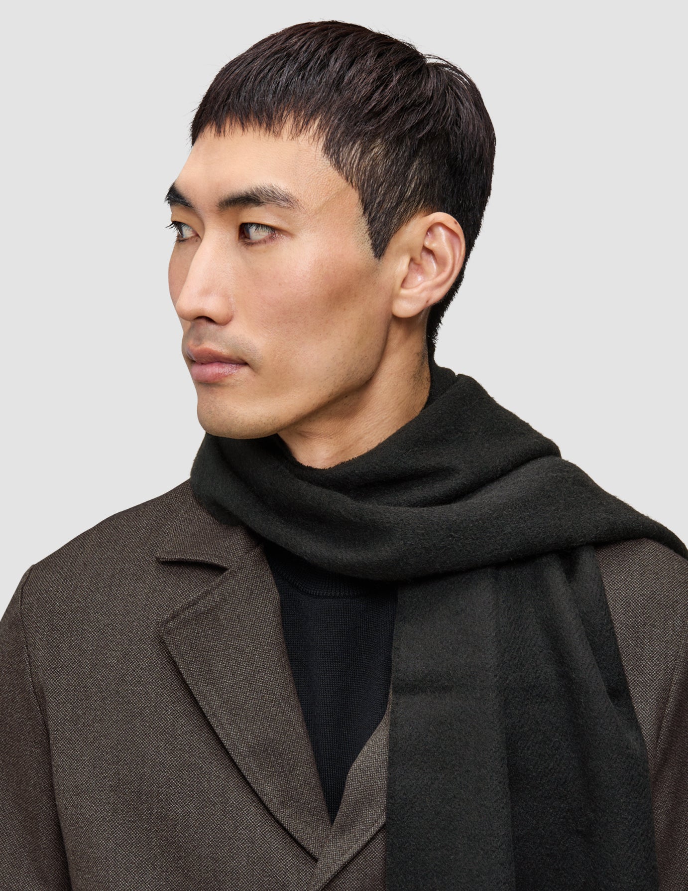En mand bærer et anderledes jakkesæt bestående af en brun Atelier Overshirt over en sort merino-striktrøje og et mørkt tørklæde.