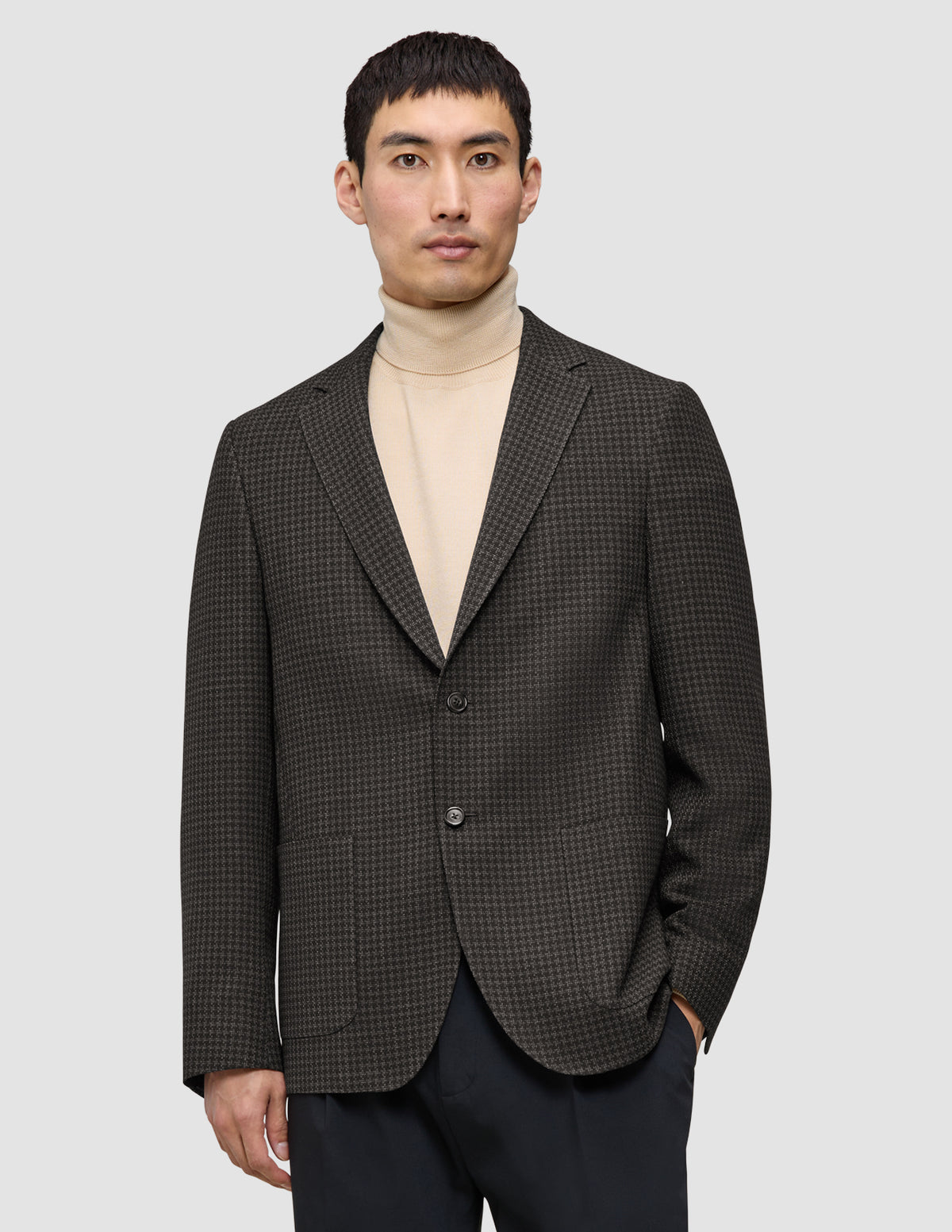 En mand iført en mørkebrun, slim-fit Timeless Wool Blazer med tern over en beige rullekravebluse.