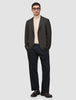En mand har en mørkebrun, slim-fit Timeless-uldsblazer med tern på, over en beige rullekravebluse og mørke bukser.