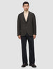 En person iført en mørkebrun, slim-fit Timeless Wool Blazer med tern over en beige rullekravebluse og mørke bukser.