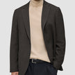En mand har en mørkebrun, slim-fit Timeless-uldblazer med tern på over en beige rullekravesweater og sorte bukser.