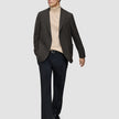 En mand har en mørkebrun, slim-fit Timeless-uldsblazer med tern på over en beige rullekravebluse og mørke bukser.