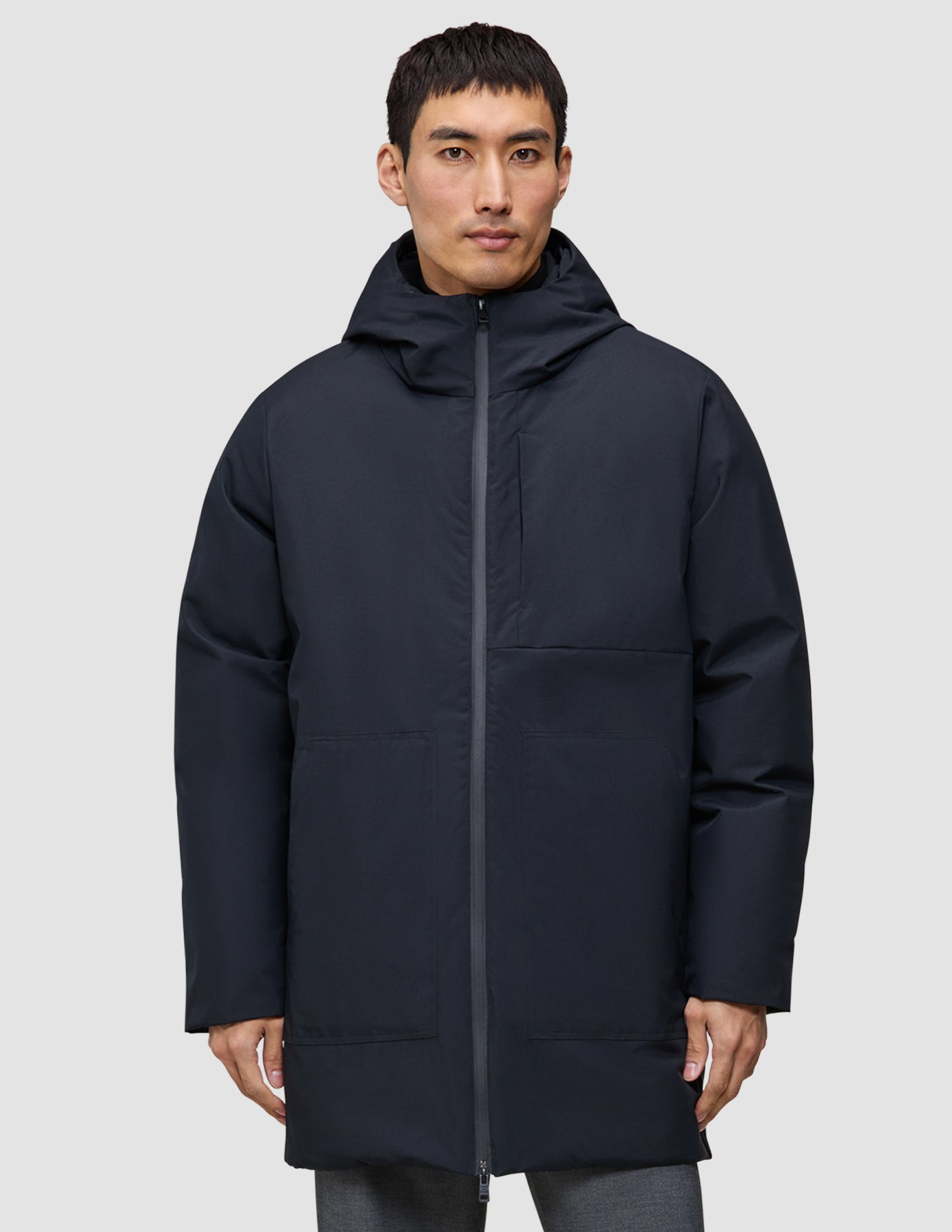 En mand iført en sort, knælængde Utility Jacket Black med hætte, fremstillet af genanvendt polyester.