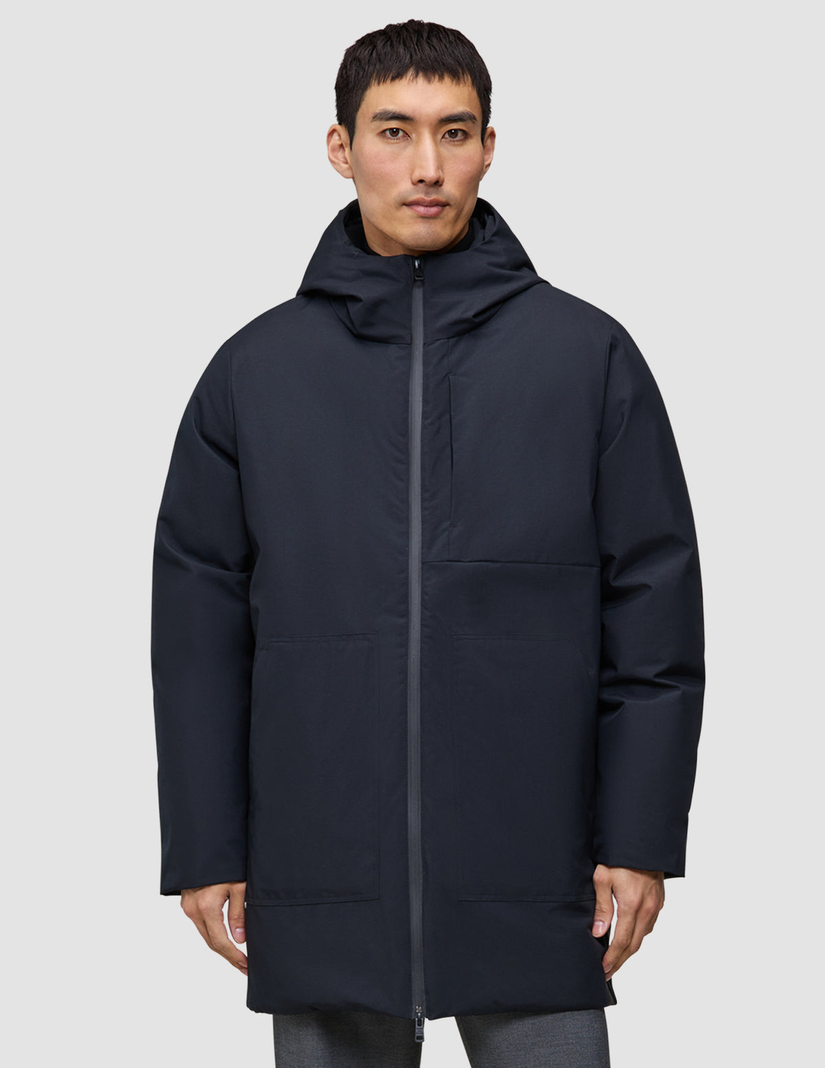 En mand iført en sort, knælængde Utility Jacket Black med hætte, fremstillet af genanvendt polyester.