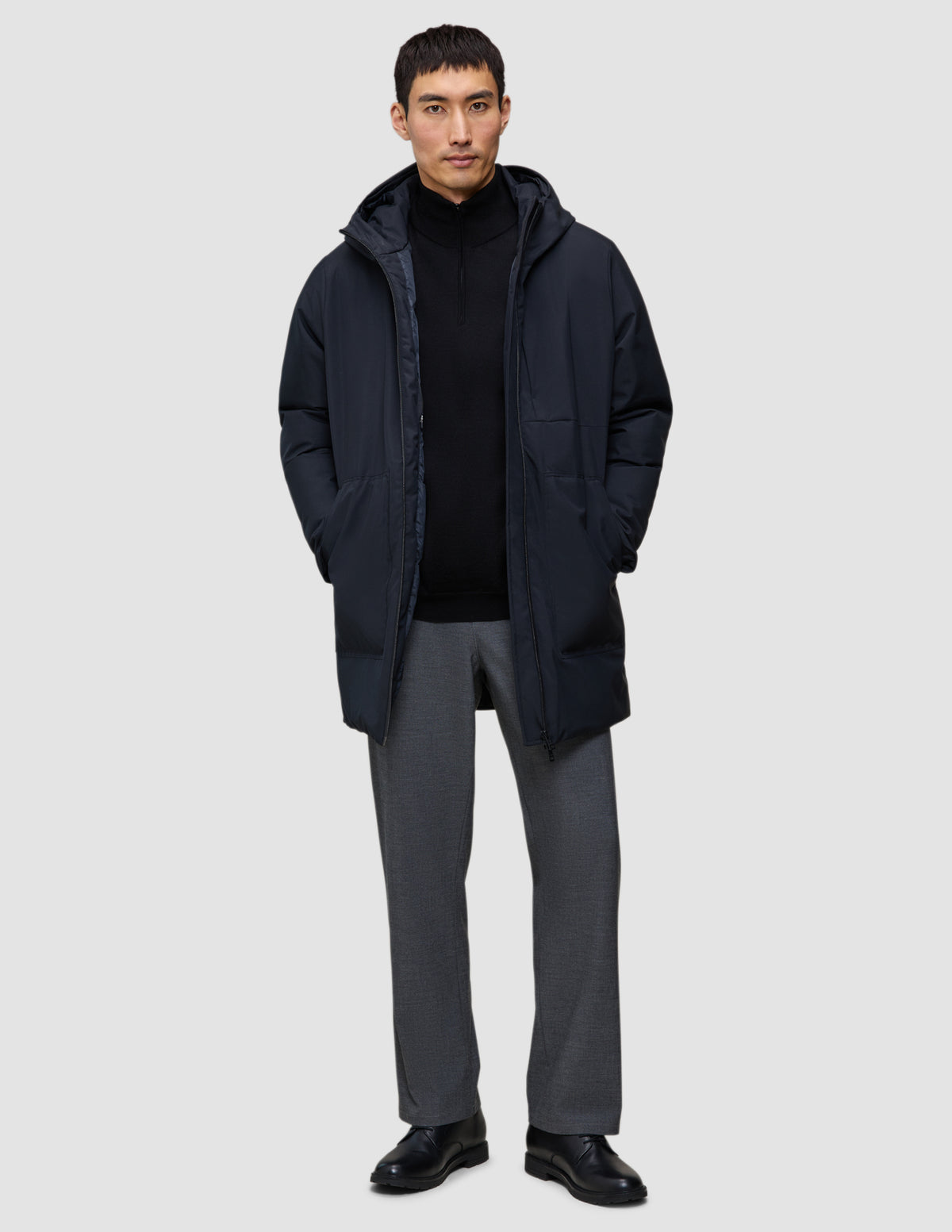 En mand iført en sort Utility-jakke over en sort sweater med kvartlængde lynlås og grå bukser.