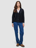 En kvinde iført en sort, tyk, blød uldstrikket cardigan fra serien Women over en hvid skjorte med krave og blå jeans.
