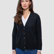 En kvinde iført en sort, tyk, blød uldstrikket cardigan fra serien Women over en hvid skjorte med krave og blå jeans.