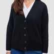 En person, der har en sort, tyk, blød uldstrikket cardigan til kvinder på over en hvid skjorte med krave og blå jeans.