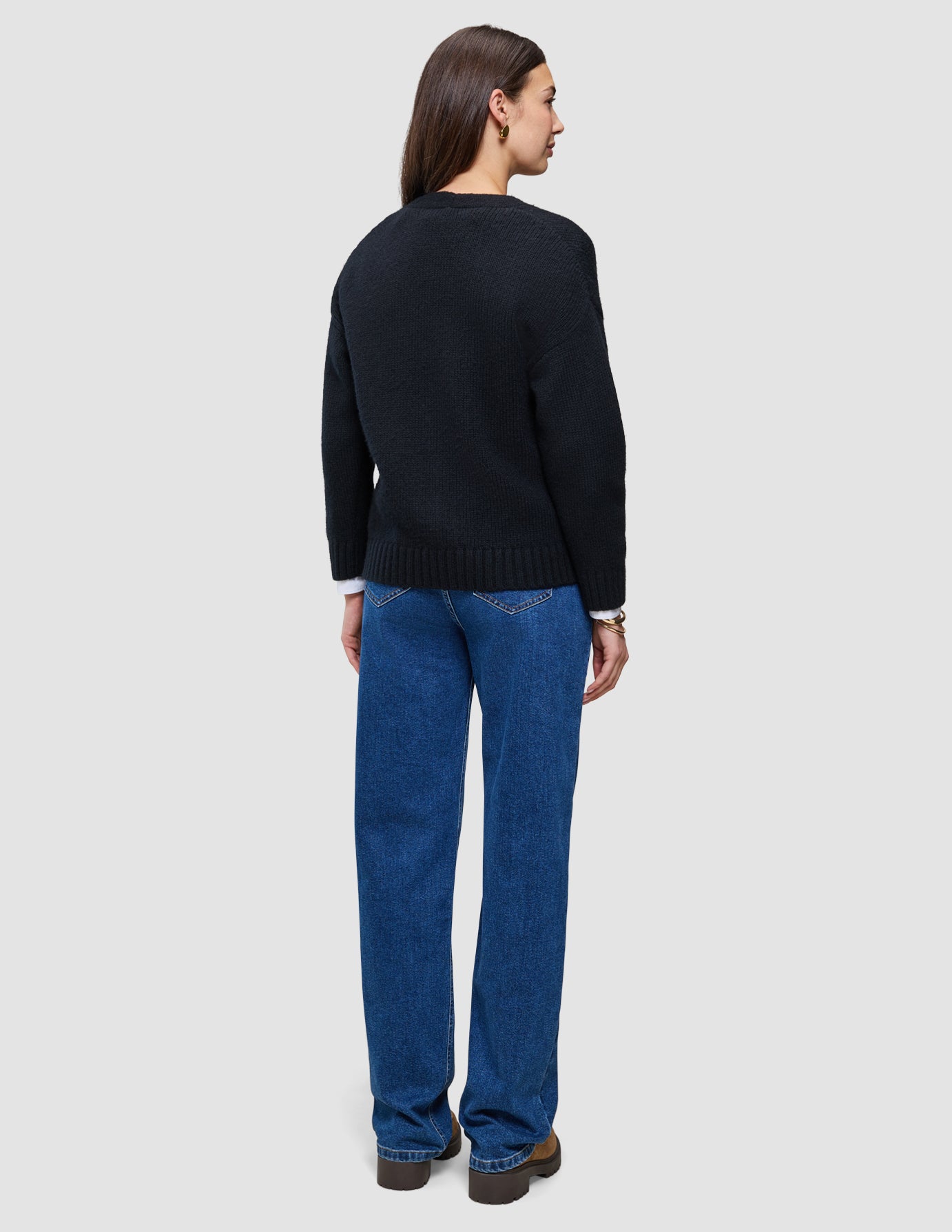 Set bagfra har personen en sort, tyk, blød uldstrikket cardigan til kvinder på over en hvid skjorte og blå jeans.