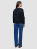 Set bagfra har personen en sort, tyk, blød uldstrikket cardigan til kvinder på over en hvid skjorte og blå jeans.