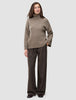 En kvinde iført en Women Chunky Soft Wool Knit Turtleneck Taupe Melange-trøje og mørkebrune bukser med tynde striber.