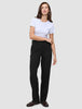Kvinde i en hvid T-shirt, Women GO2-bukser i lige snit i sort og mørke loafers.