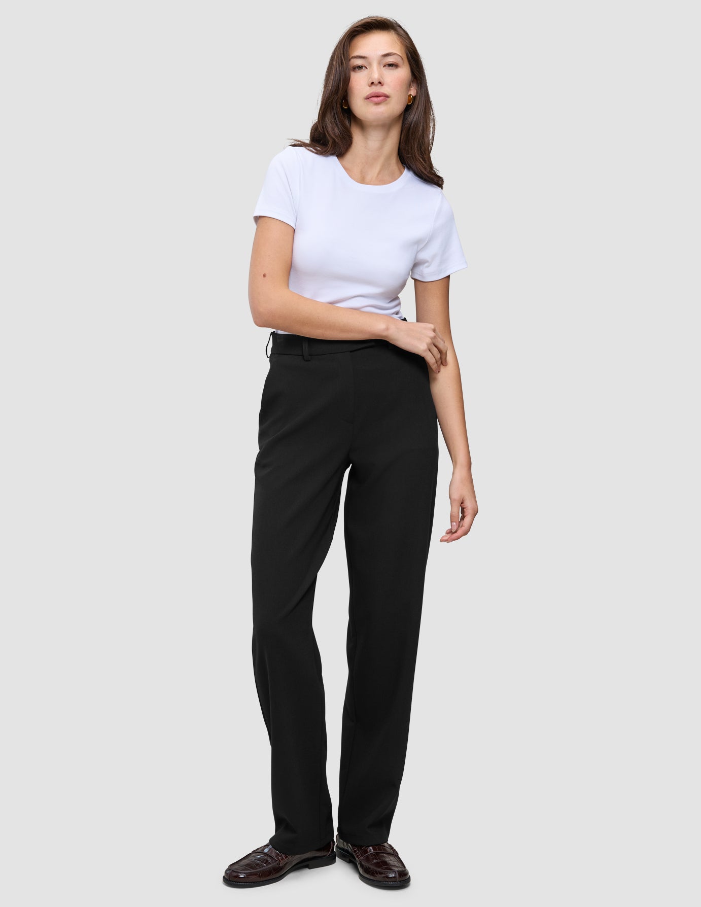 Kvinde i en hvid T-shirt, Women GO2-bukser i lige snit i sort og mørke loafers.