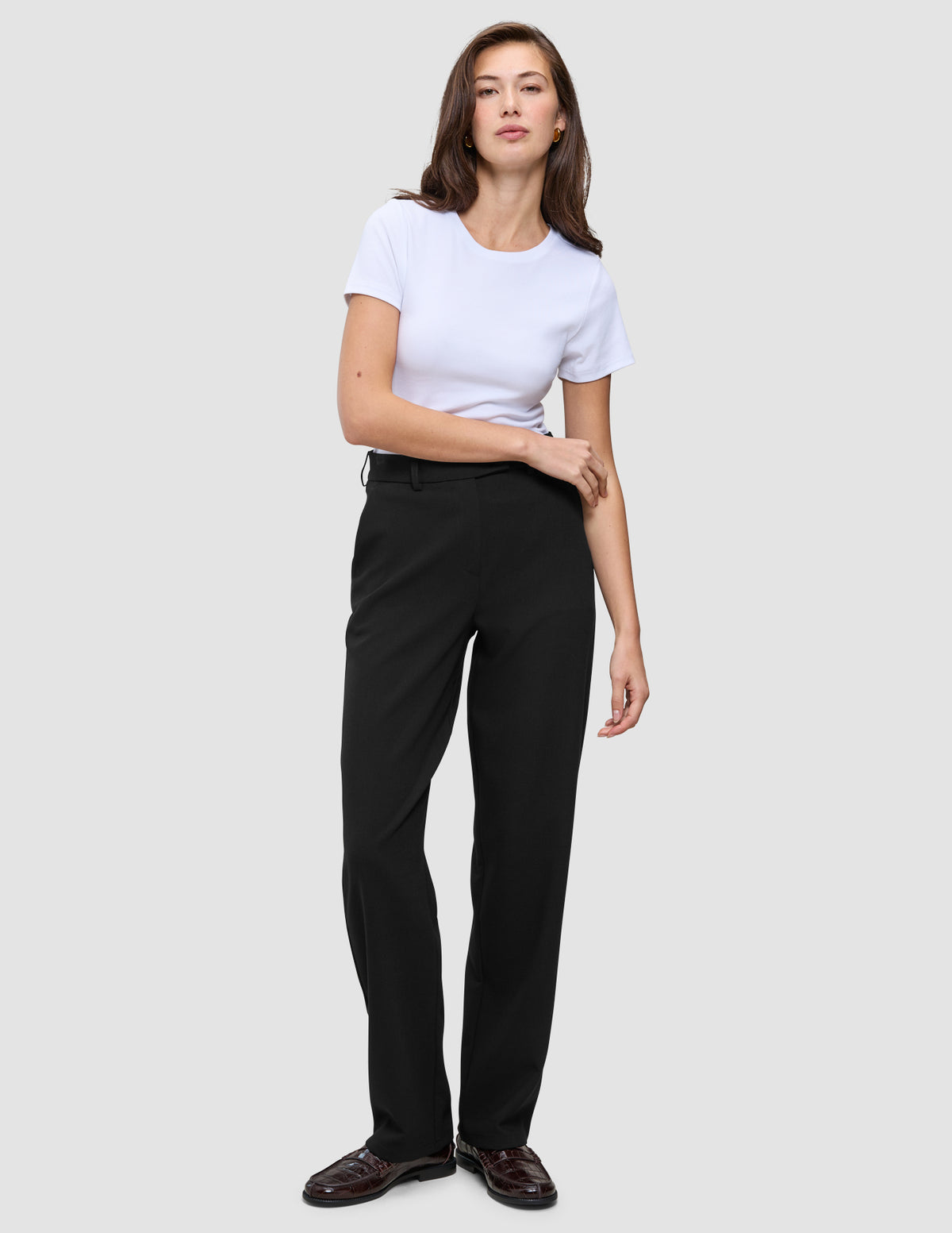 Kvinde i en hvid T-shirt, Women GO2-bukser i lige snit i sort og mørke loafers.