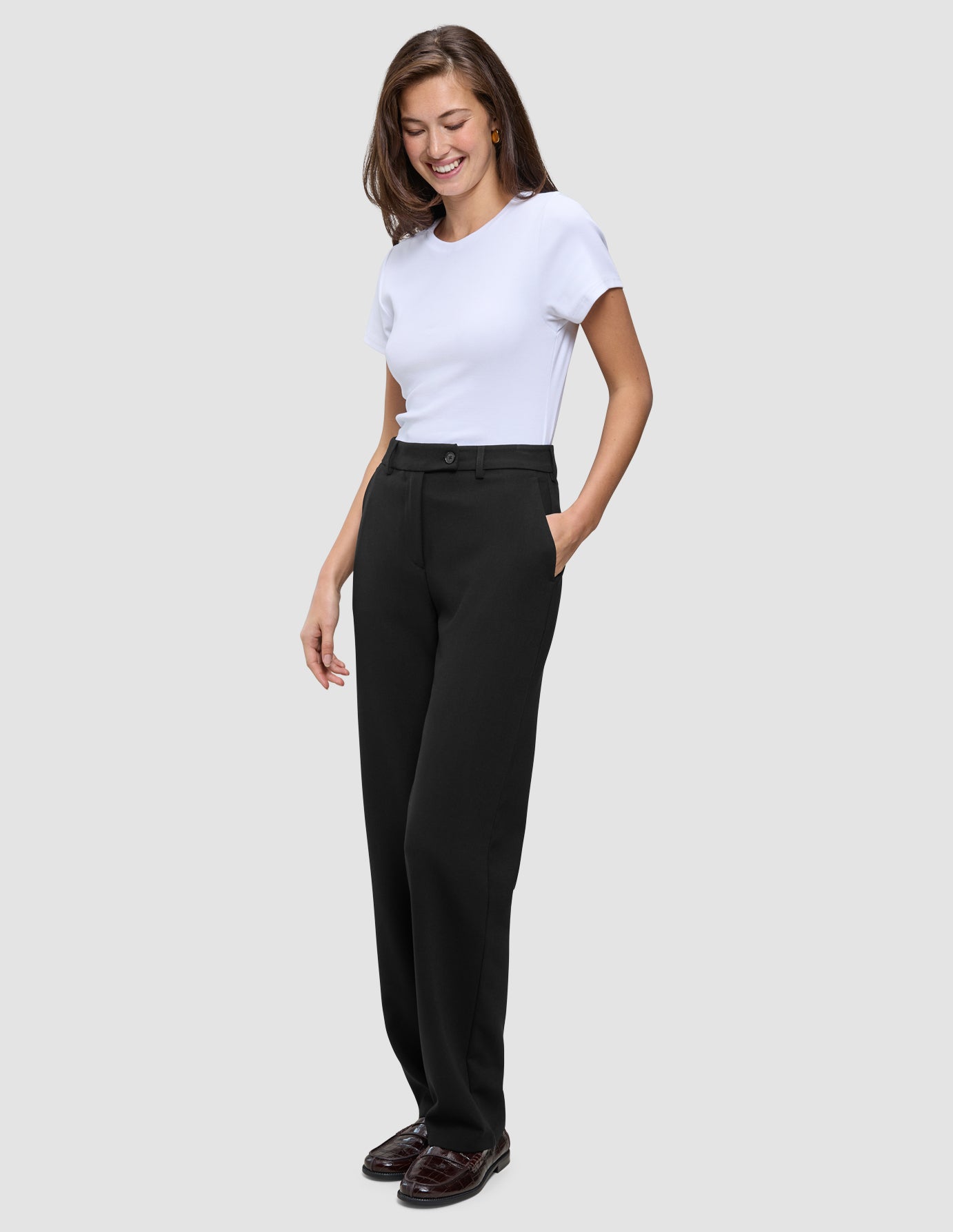 En kvinde iført en hvid T-shirt og sorte, lige Women GO2-bukser med hånden i lommen.