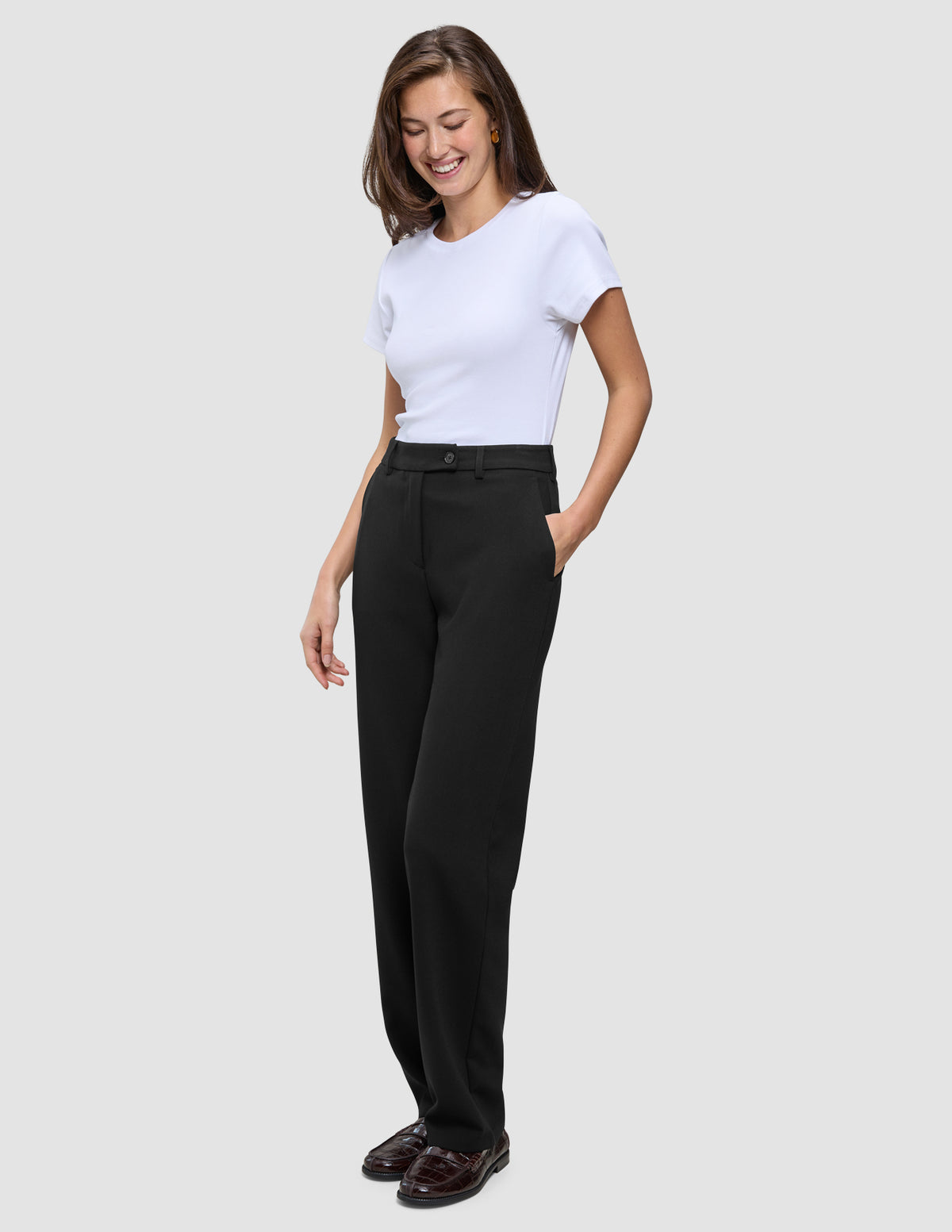 En kvinde iført en hvid T-shirt og sorte, lige Women GO2-bukser med hånden i lommen.