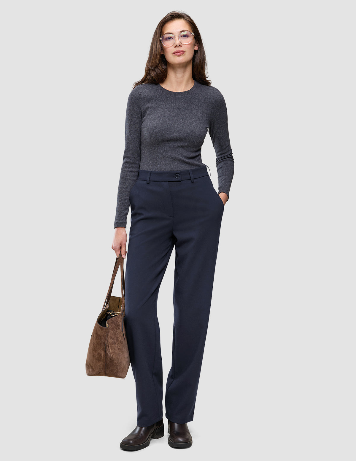 En kvinde i en grå langærmet bluse har Women GO2 Pants Straight Blue Nights på og holder en brun håndtaske.