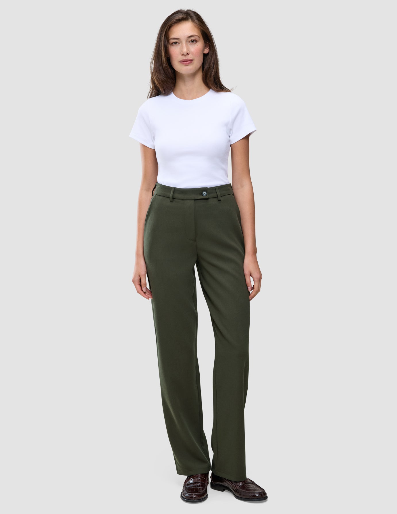 En kvinde i en hvid T-shirt, der er stukket ned i et par olivengrønne Women GO2-bukser i straight-fit i farven Dusty Olive, og mørke loafers.