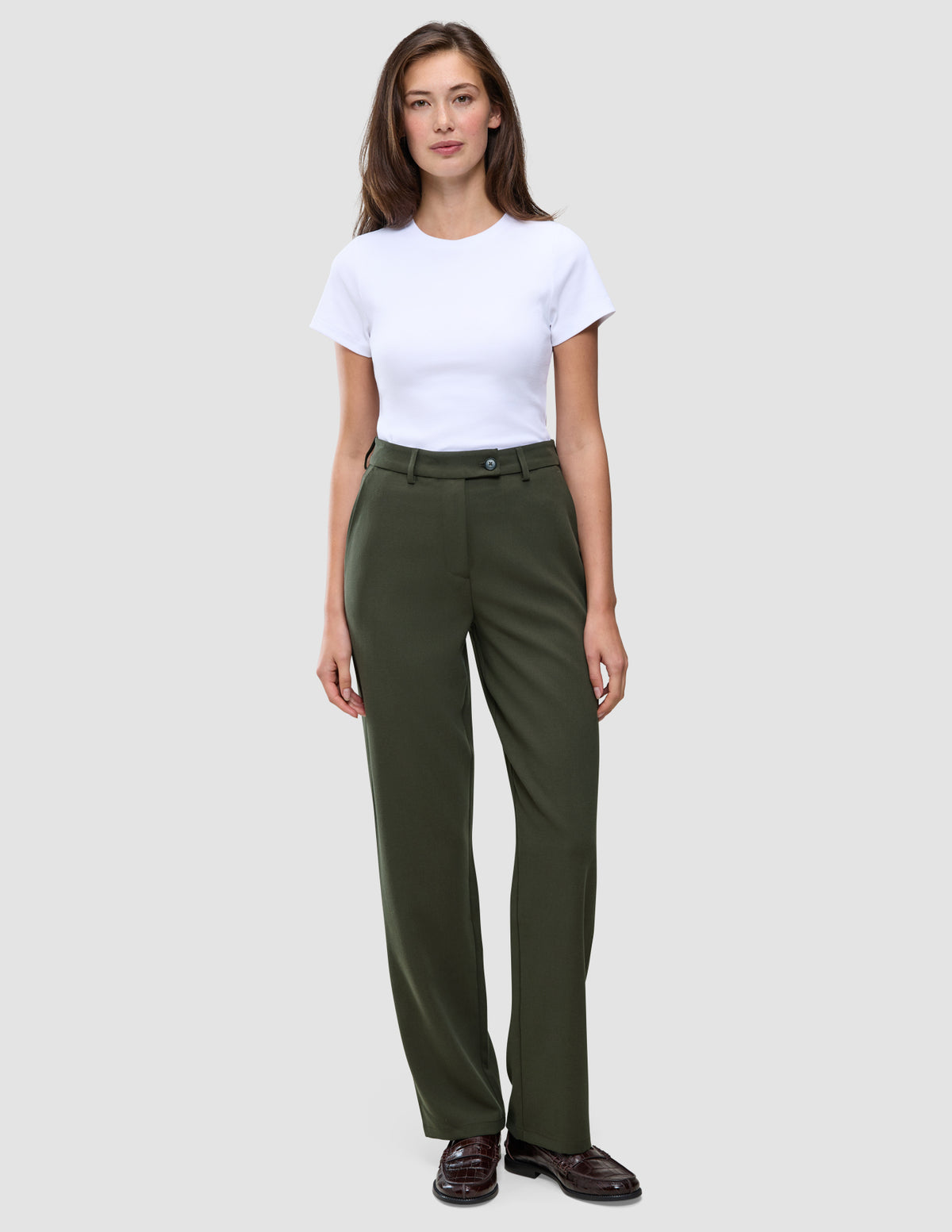 En kvinde i en hvid T-shirt, der er stukket ned i et par olivengrønne Women GO2-bukser i straight-fit i farven Dusty Olive, og mørke loafers.