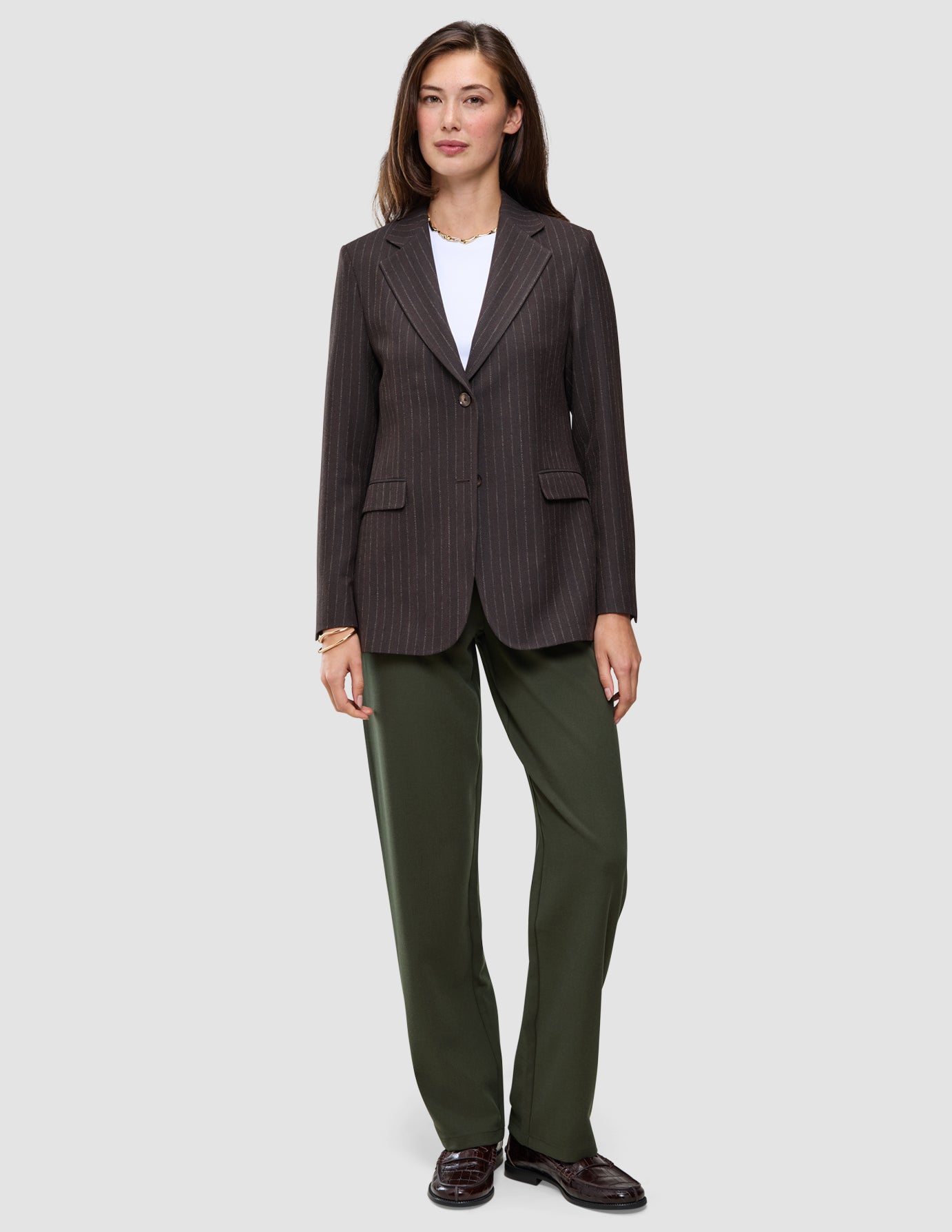 En kvinde har en brun blazer med tynde striber på over en hvid T-shirt og et par Women GO2-bukser i model Straight i farven Dusty Olive.