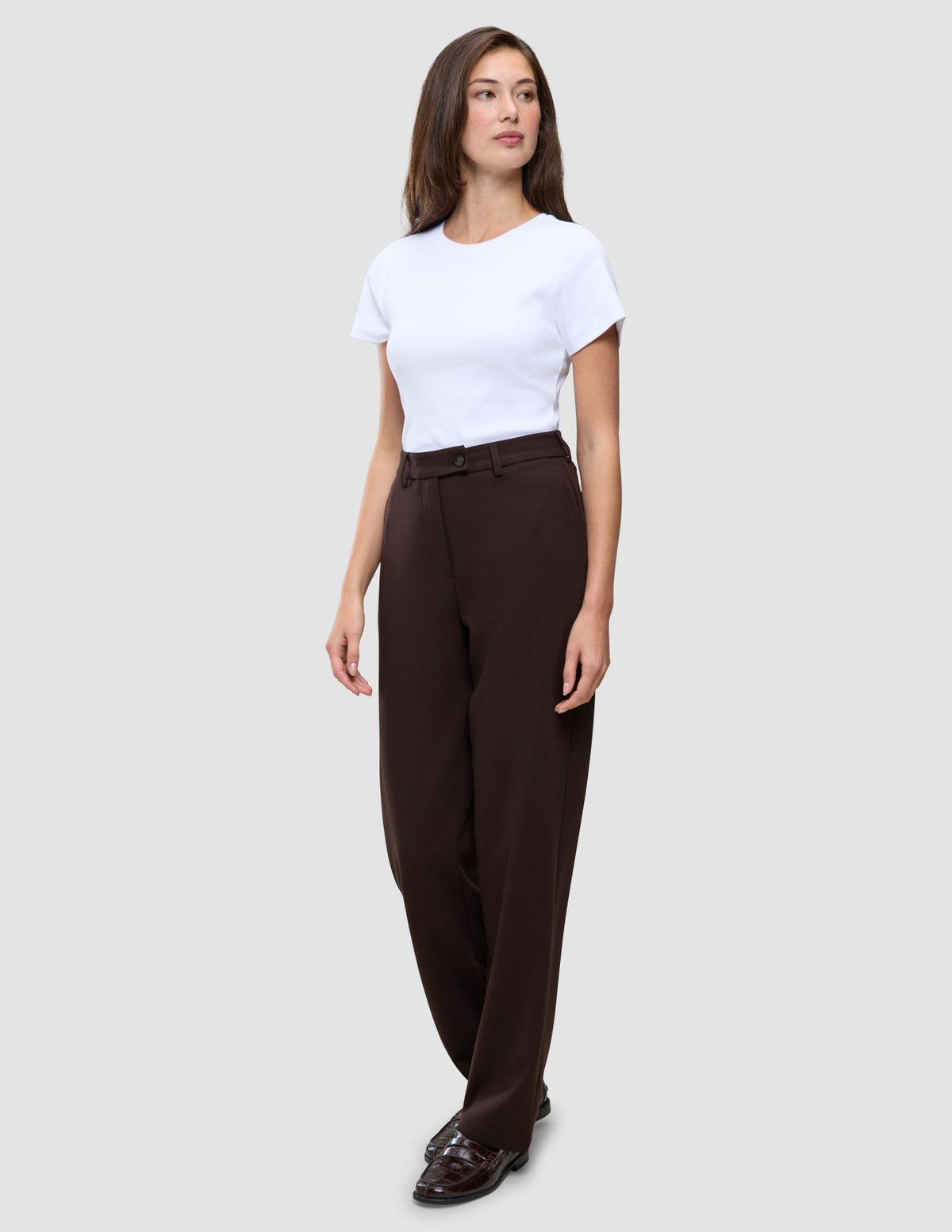 En kvinde iført en hvid T-shirt, mørkebrune Women GO2 Pants Straight Mocha og loafers.