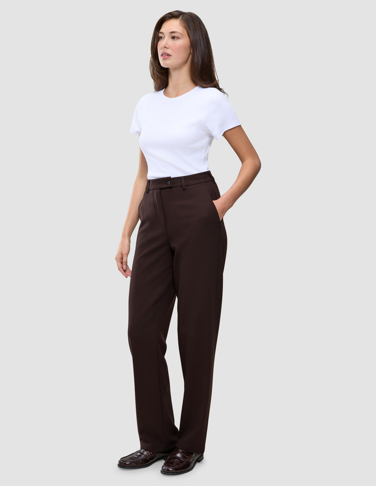 En kvinde i en hvid T-shirt og et par Women GO2 Pants Straight Mocha med hånden i lommen.