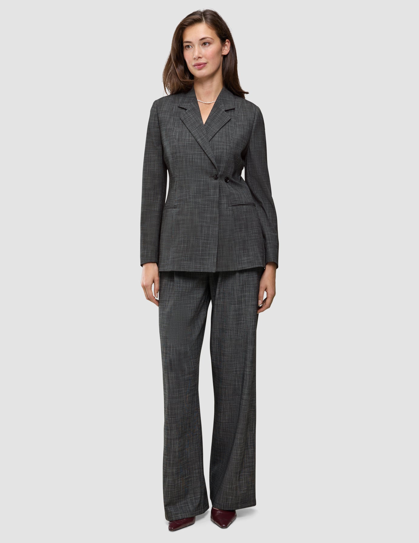 En kvinde er klædt i en koksgrå Women Nara Blazer Fitted Black Check og bukser med brede ben, der er et udtryk for elegant dansk design.
