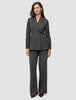 En kvinde er klædt i en koksgrå Women Nara Blazer Fitted Black Check og bukser med brede ben, der er et udtryk for elegant dansk design.