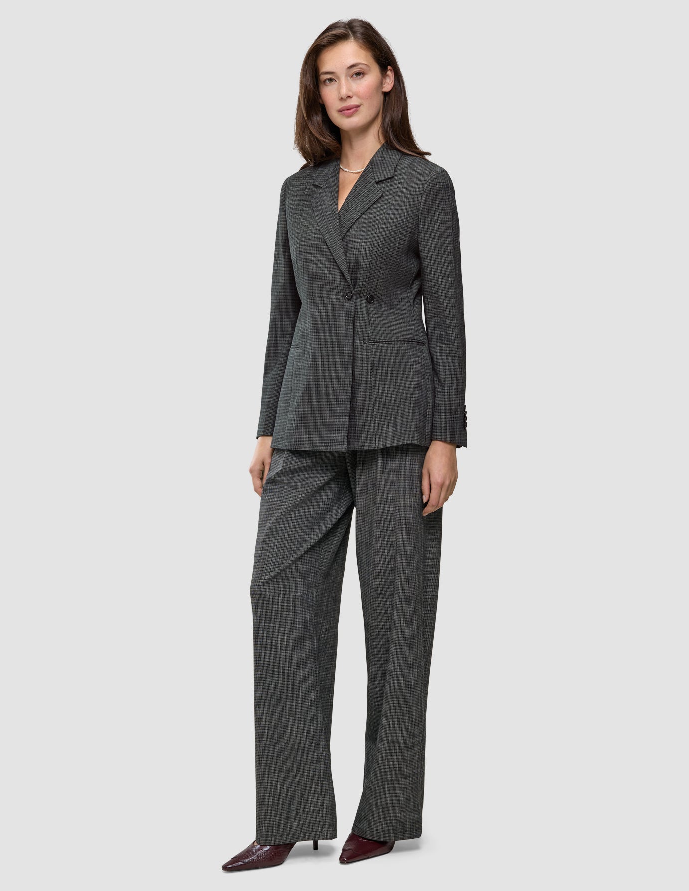 En kvinde har den tætsiddende Nara-blazer til kvinder i sort ternet mønster på, sammen med et par matchende bukser med brede ben og 360°-stretch.