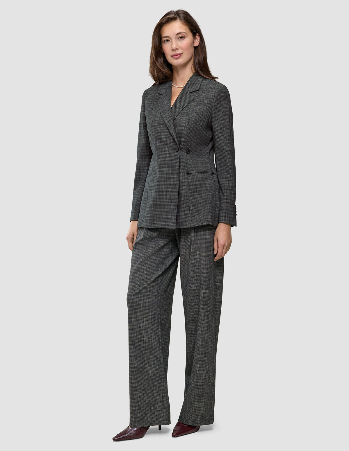 En kvinde har den tætsiddende Nara-blazer til kvinder i sort ternet mønster på, sammen med et par matchende bukser med brede ben og 360°-stretch.