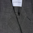 Nærbillede af en sort-hvid ternet Women Nara Blazer Fitted Black Check med et SHAPING NEW TOMORROW-mærke ved halsudskæringen.