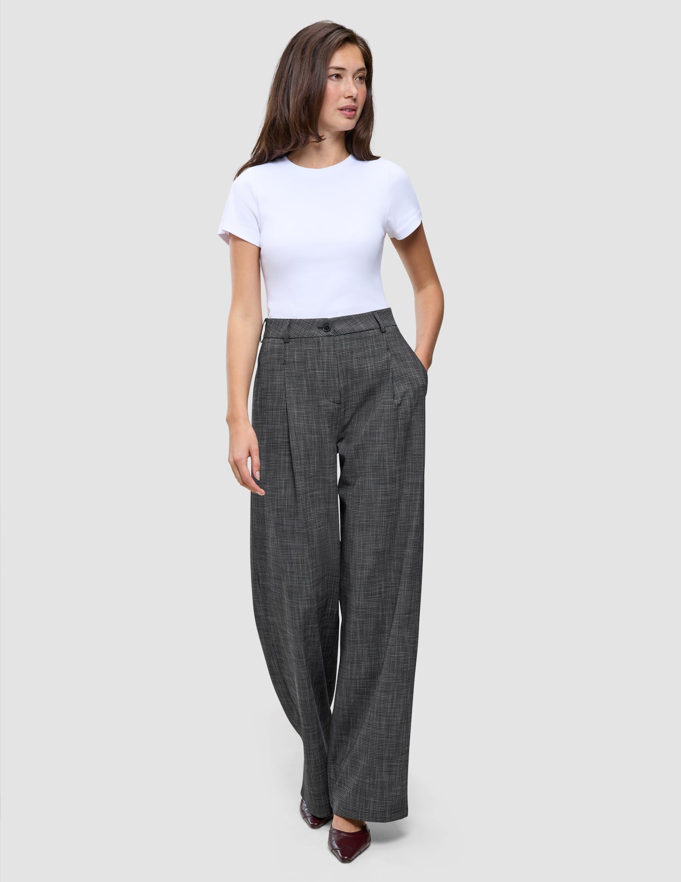 Kvinde iført en hvid T-shirt og Nara-bukser i bred pasform med sort ternet mønster.