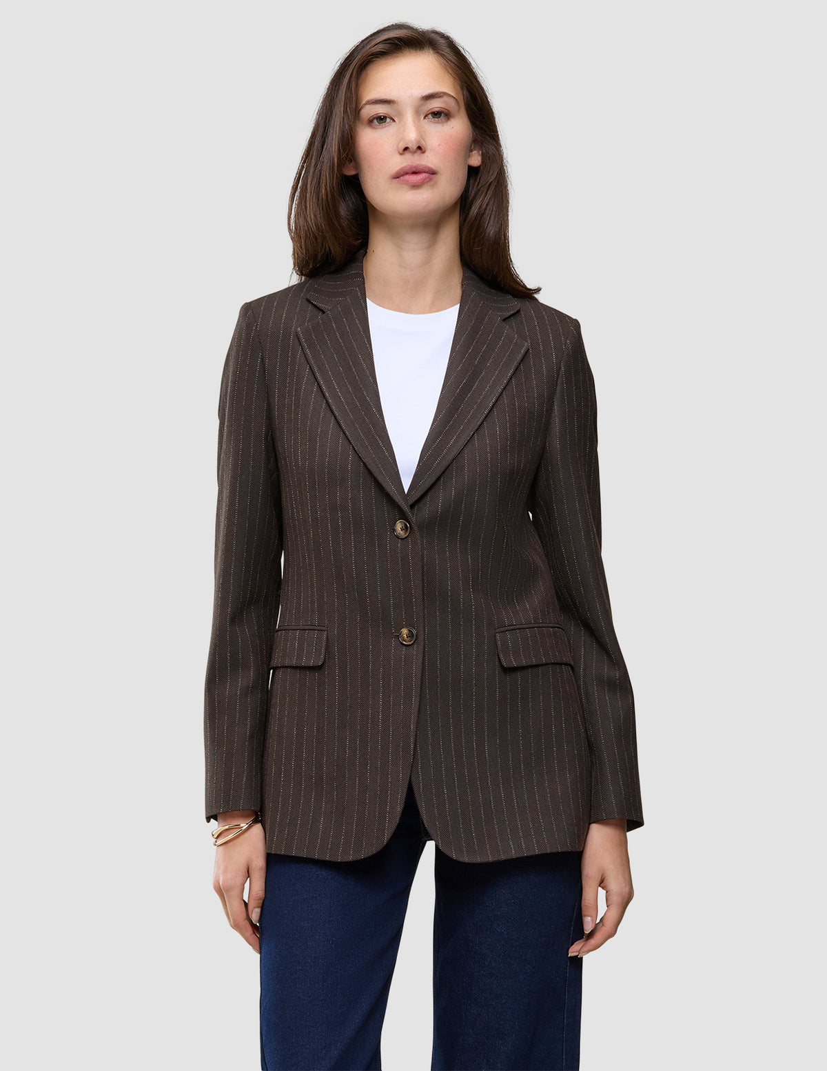 En kvinde iført en Women Serene Blazer Regular Walnut Herringbone over en hvid T-shirt og blå jeans.
