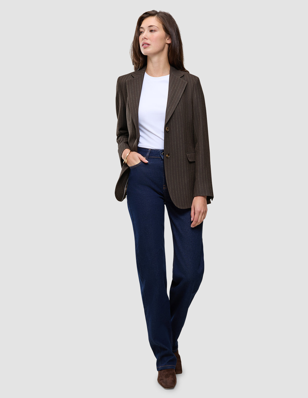 En person, der har en brun Women Serene Blazer Regular Walnut Herringbone på over en hvid T-shirt og blå jeans.