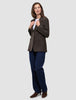 En kvinde har en brun Women Serene Blazer Regular Walnut Herringbone på over en hvid T-shirt, blå jeans og brune støvler.