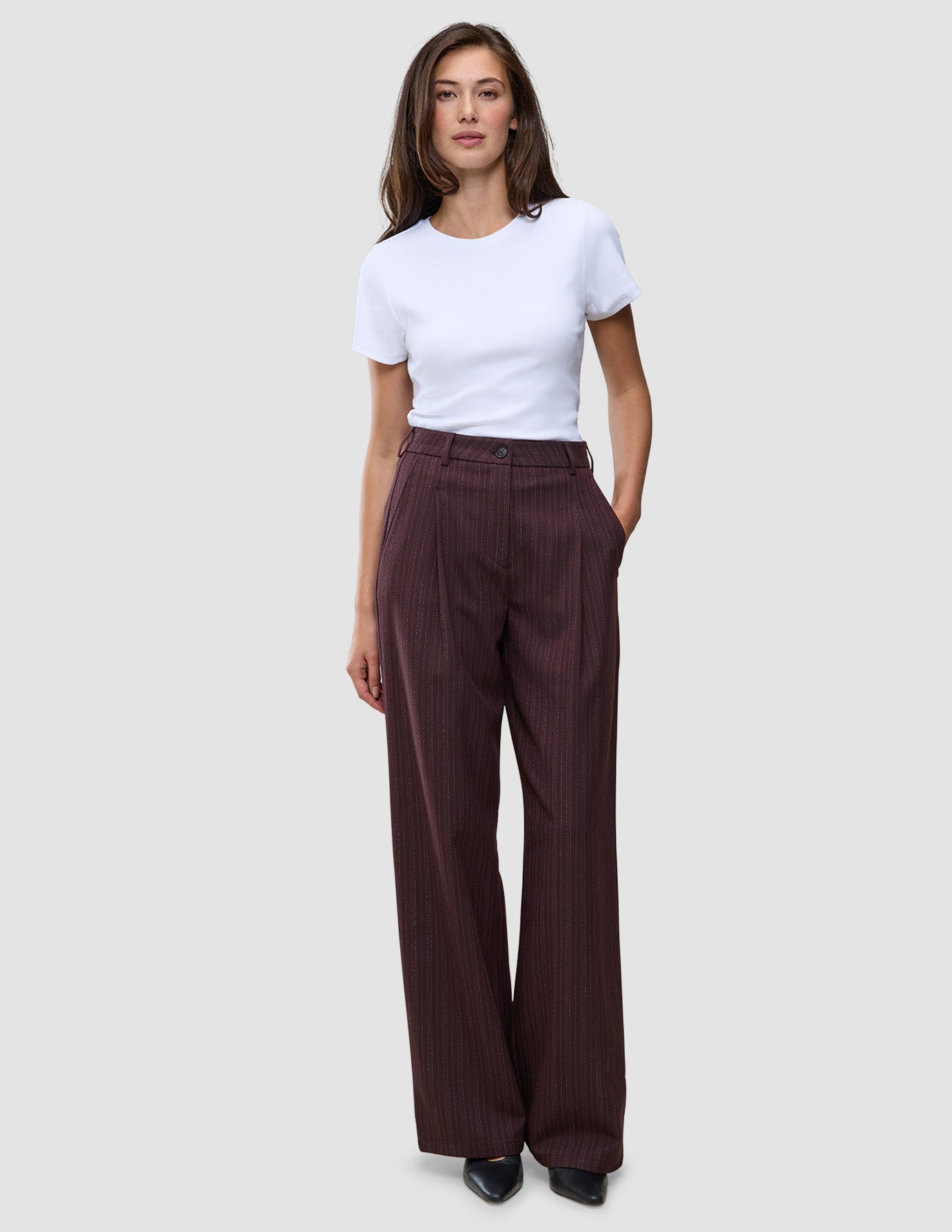 En kvinde iført en hvid T-shirt og et par Women Serene Pants Wide Berry Pinstripe, som er mørkebærfarvede bukser med brede ben.
