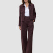 En kvinde iført et buksesæt af modellen Women Serene Pants Wide Berry Pinstripe over en hvid skjorte med krave.