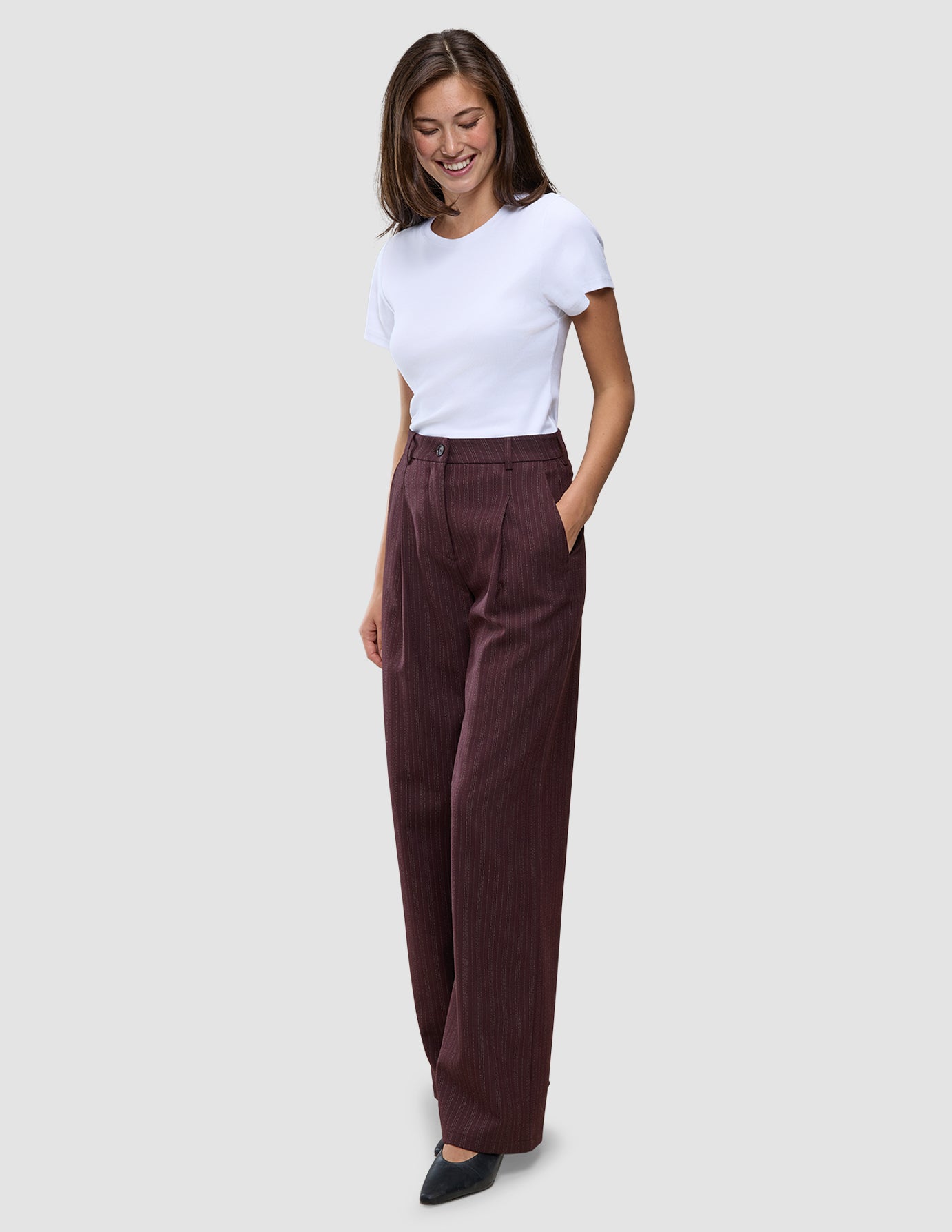 En kvinde har en hvid T-shirt på og et par Women Serene Pants Wide Berry Pinstripe med høj talje og brede ben.
