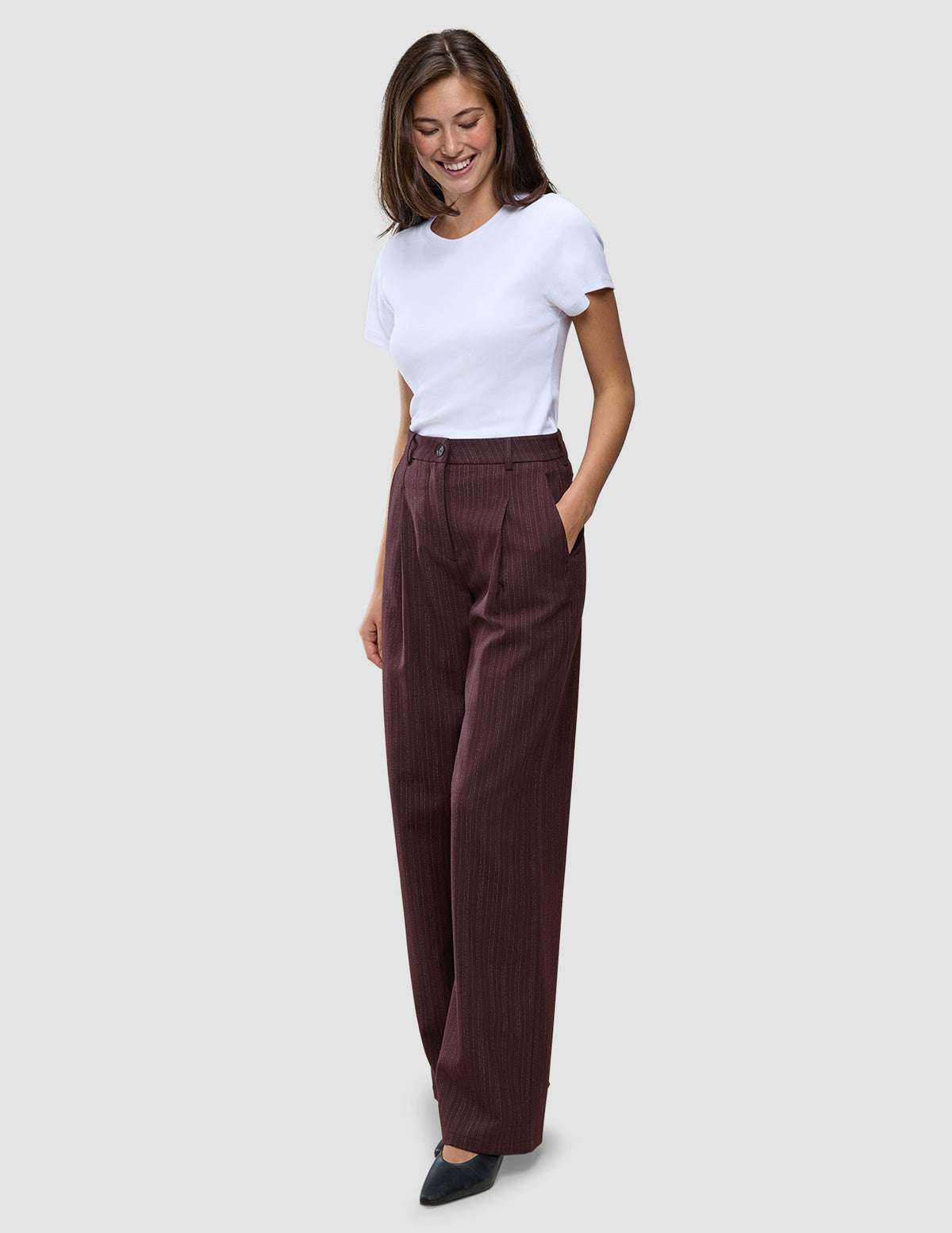 En kvinde har en hvid T-shirt på og et par Women Serene Pants Wide Berry Pinstripe med høj talje og brede ben.