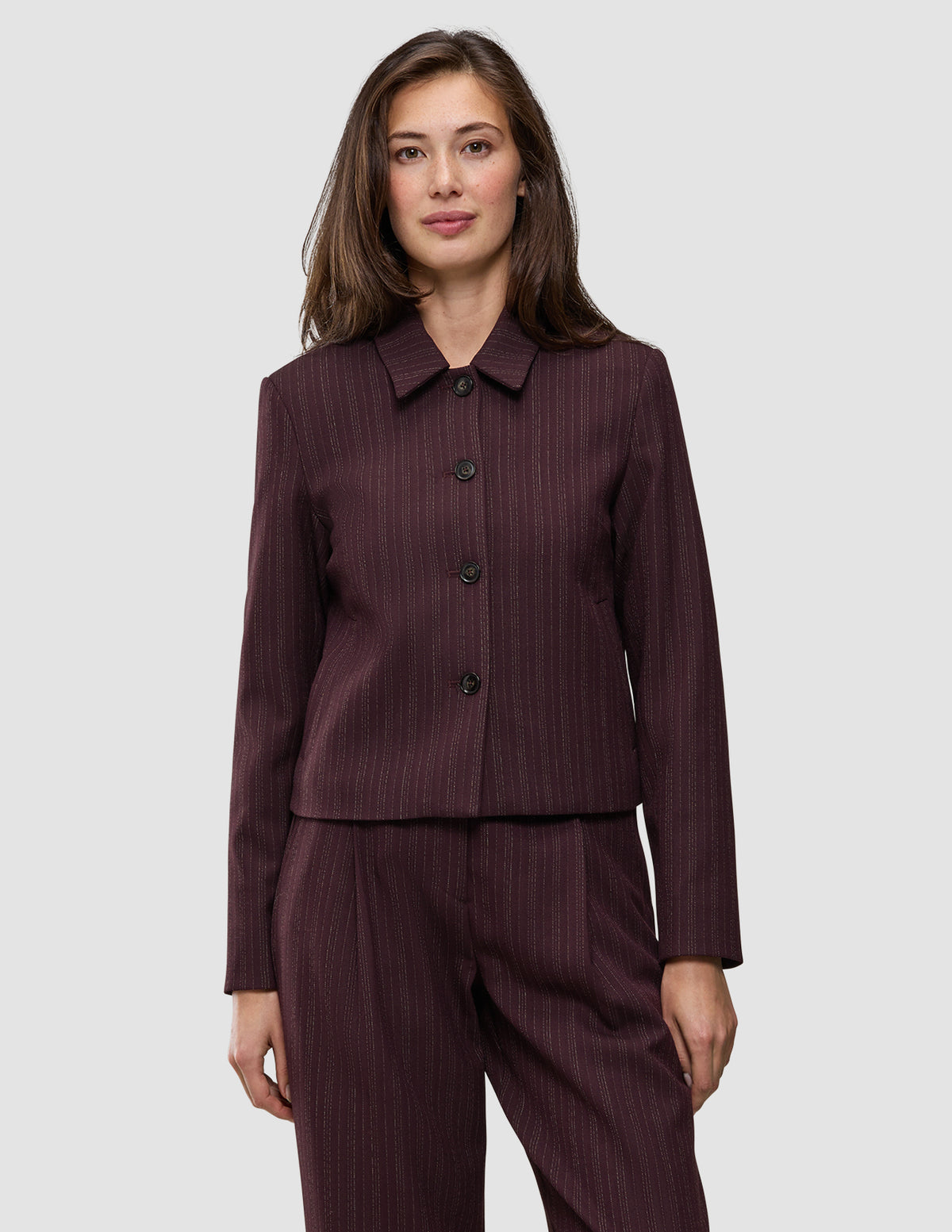 En kvinde bærer en Women Serene Short Jacket Berry Pinstripe i et mørkt bærfarvet stof med fine striber, der afspejler klassisk dansk design.