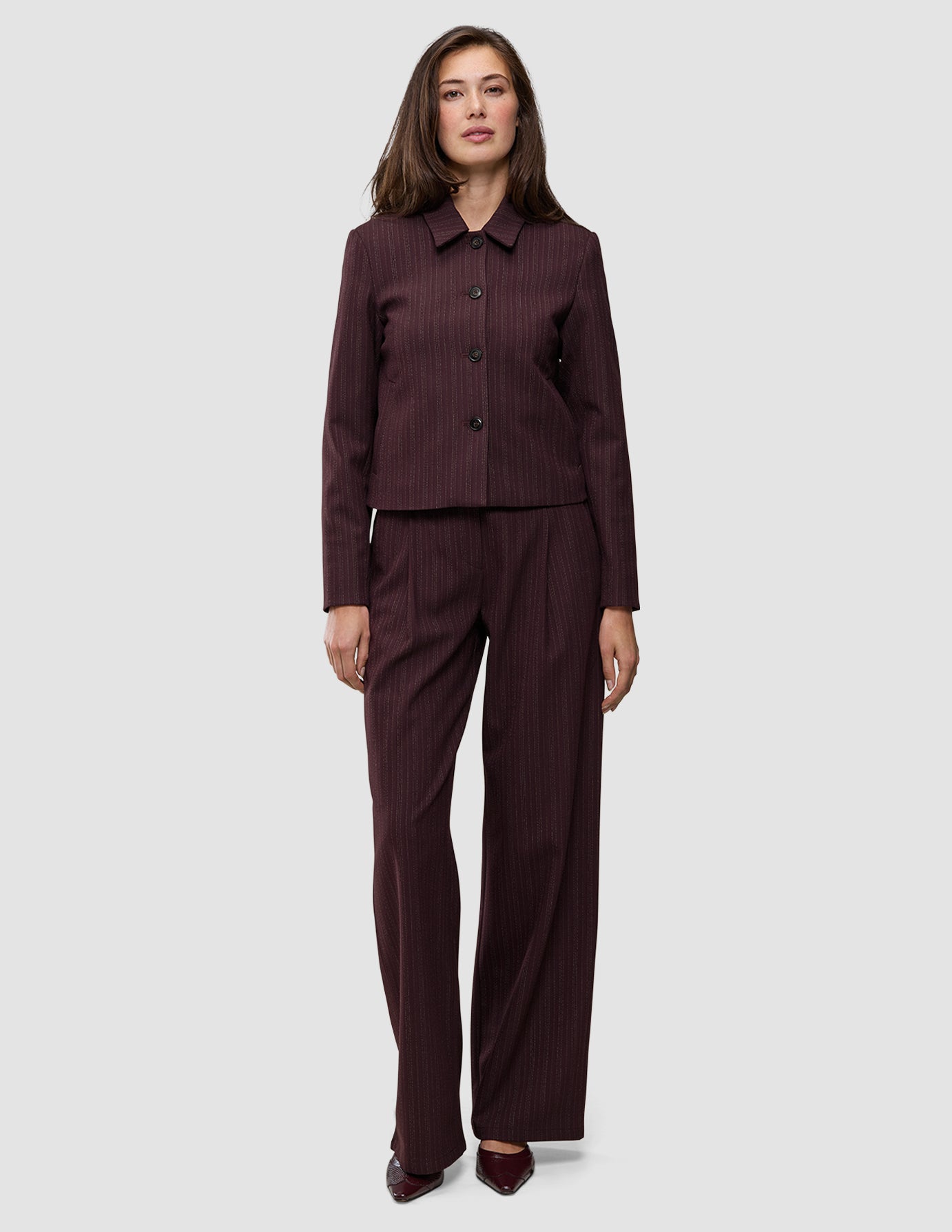 En kvinde iført en Women Serene Short Jacket i farven Berry Pinstripe og tilhørende bukser med brede ben i et minimalistisk dansk design.