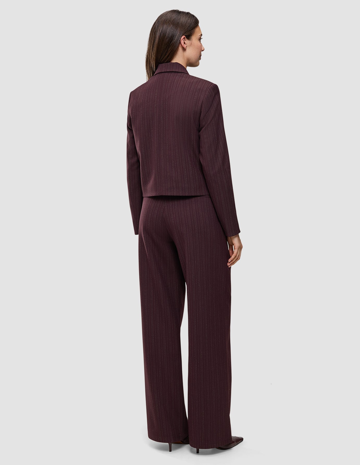 En kvinde set bagfra har den korte jakke Women Serene Short Jacket Berry Pinstripe på sammen med et par matchende bukser med brede ben.