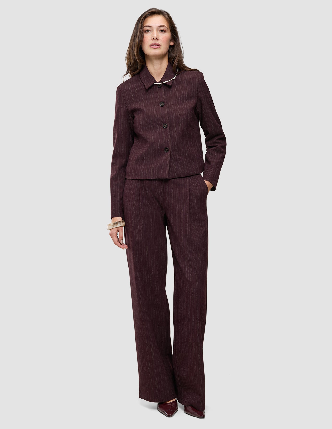 En person iført en Women Serene Short Jacket Berry Pinstripe sammen med et par matchende bukser med brede ben i dansk design.